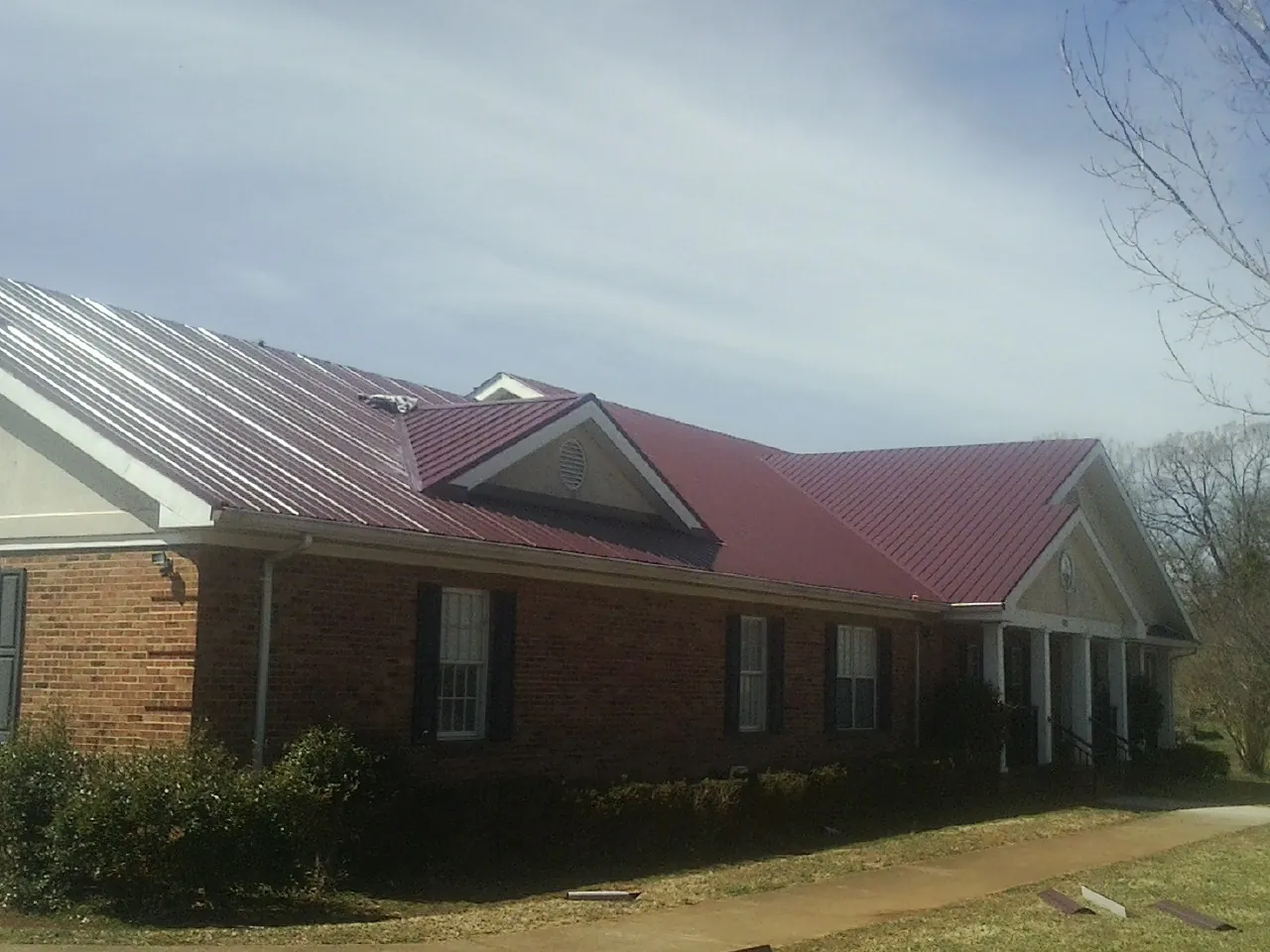 Red metal roof with gabled entries on a long brick building, from a Hail Damage Roof Repair job in Orem
