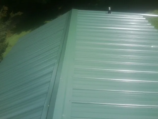 New green metal panels meeting at the ridge of a roof — Flat Roof Repair work by our crew in Orem
