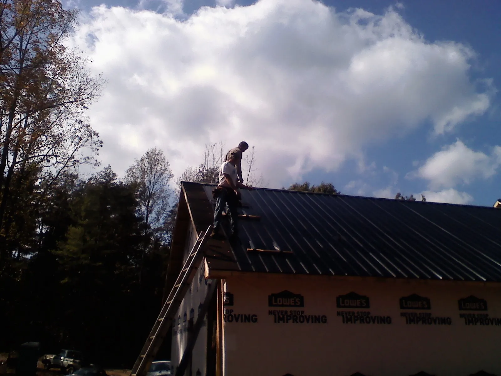 Roofer fastening dark metal panels high against a cloudy sky, from a Roof Inspection job in Orem