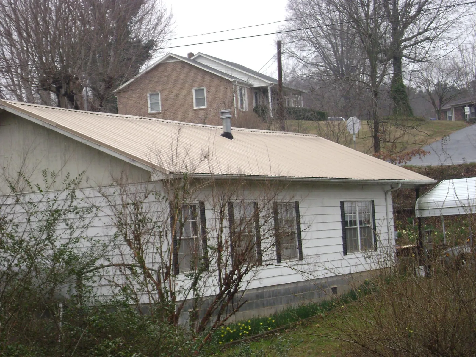 Tan metal roof on a white sided house set into a hillside — Commercial Roofing by Roofing Brothers in Orem